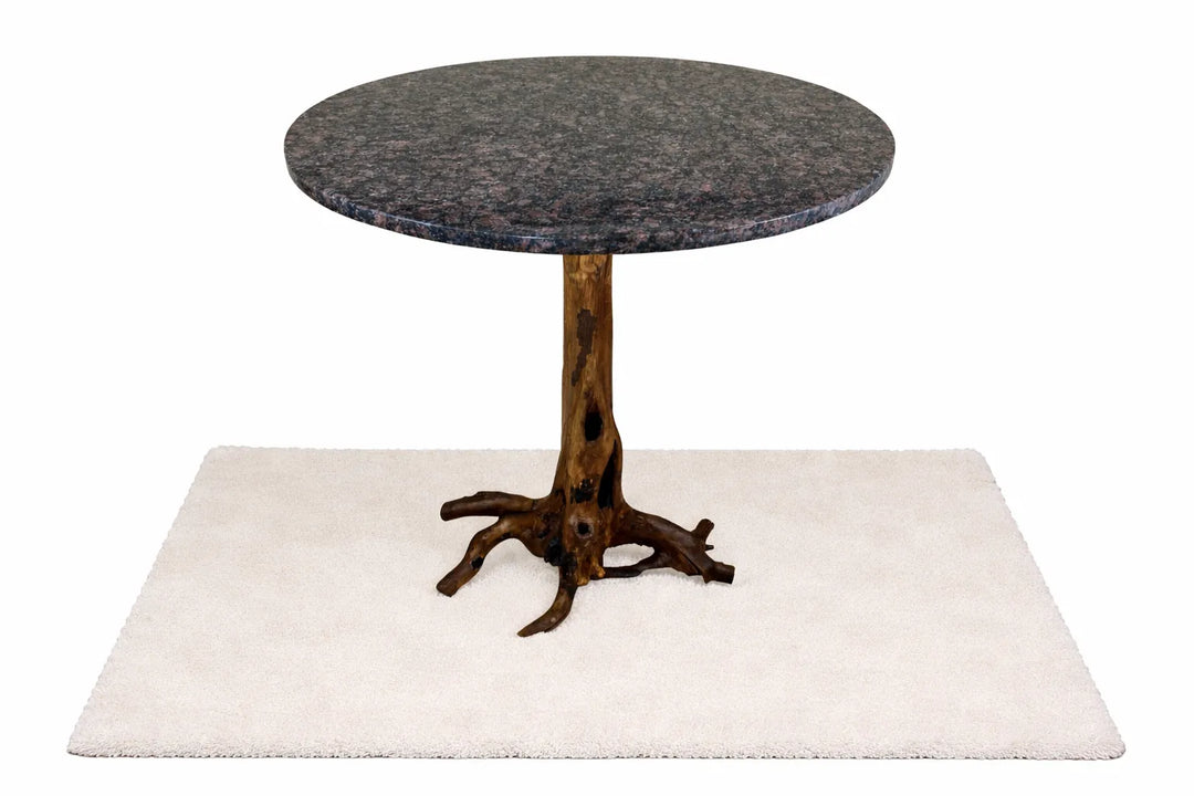 Feature view of a dark blue granite table top on a brown tree root base resting on a white rug with white background.