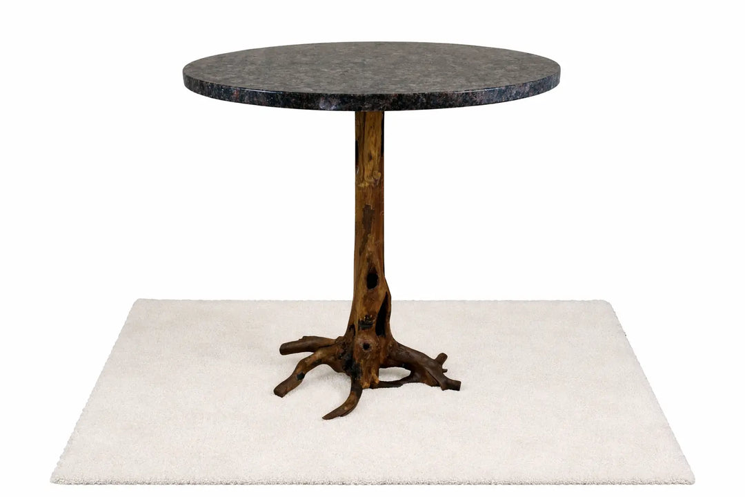 Front view of dark granite bistro dining table top on a slender brown tree stump base.  Standing on a white rug with white background.