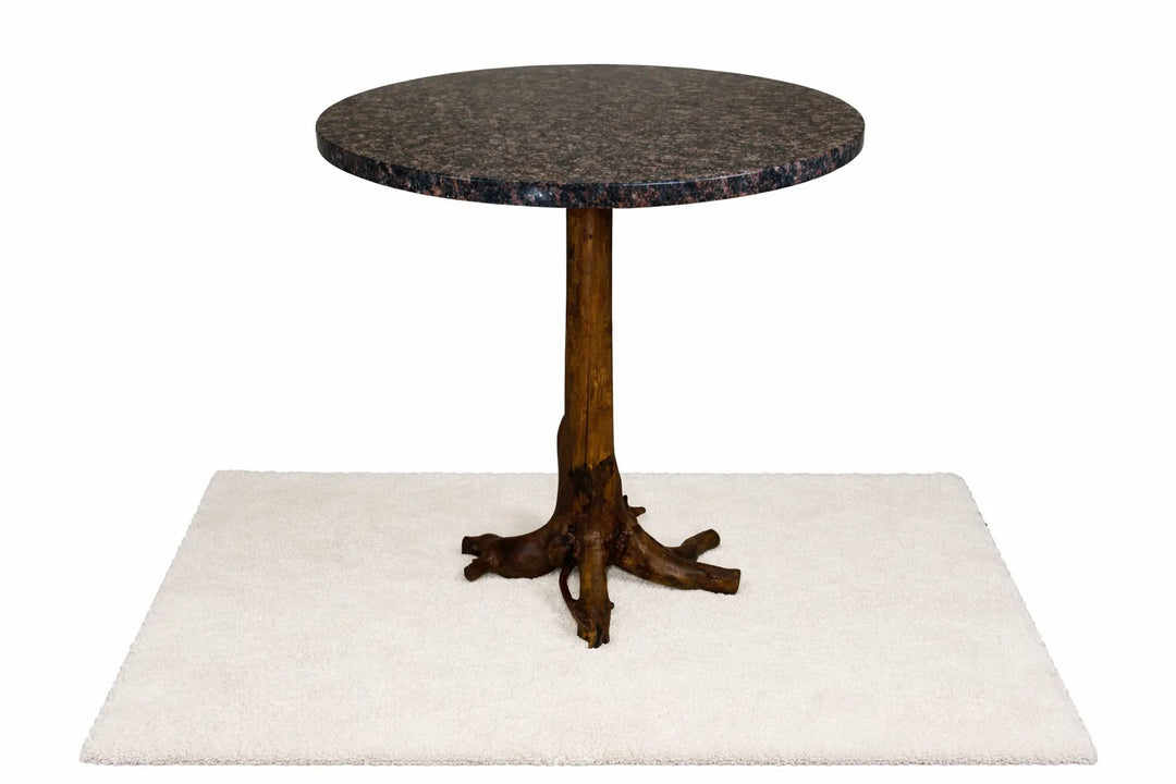 Round dark blue granite dining table mounted on a tree stump pedestal.  Standing on a white rug with white background.