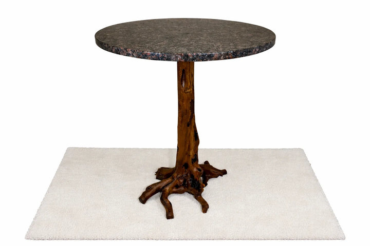 Front view of a round dark colored granite table on a tree stump pedestal on a white rug and white background.