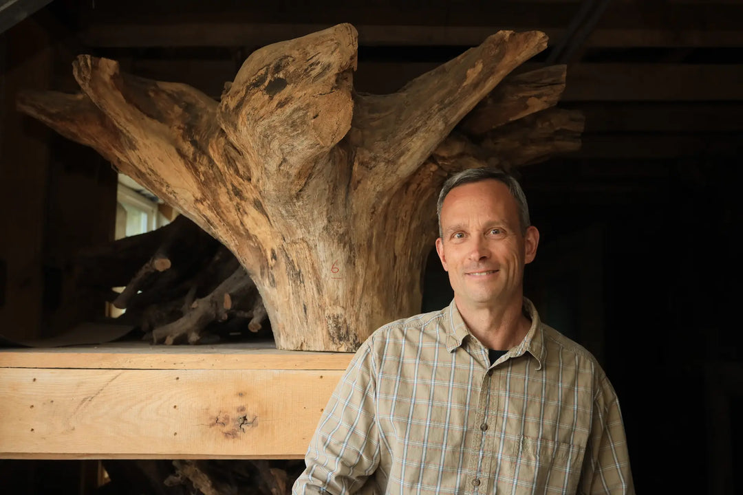 Artisan Matt Kruse standing with a dried tree stump on a shelf behind his shoulder with a black back ground.