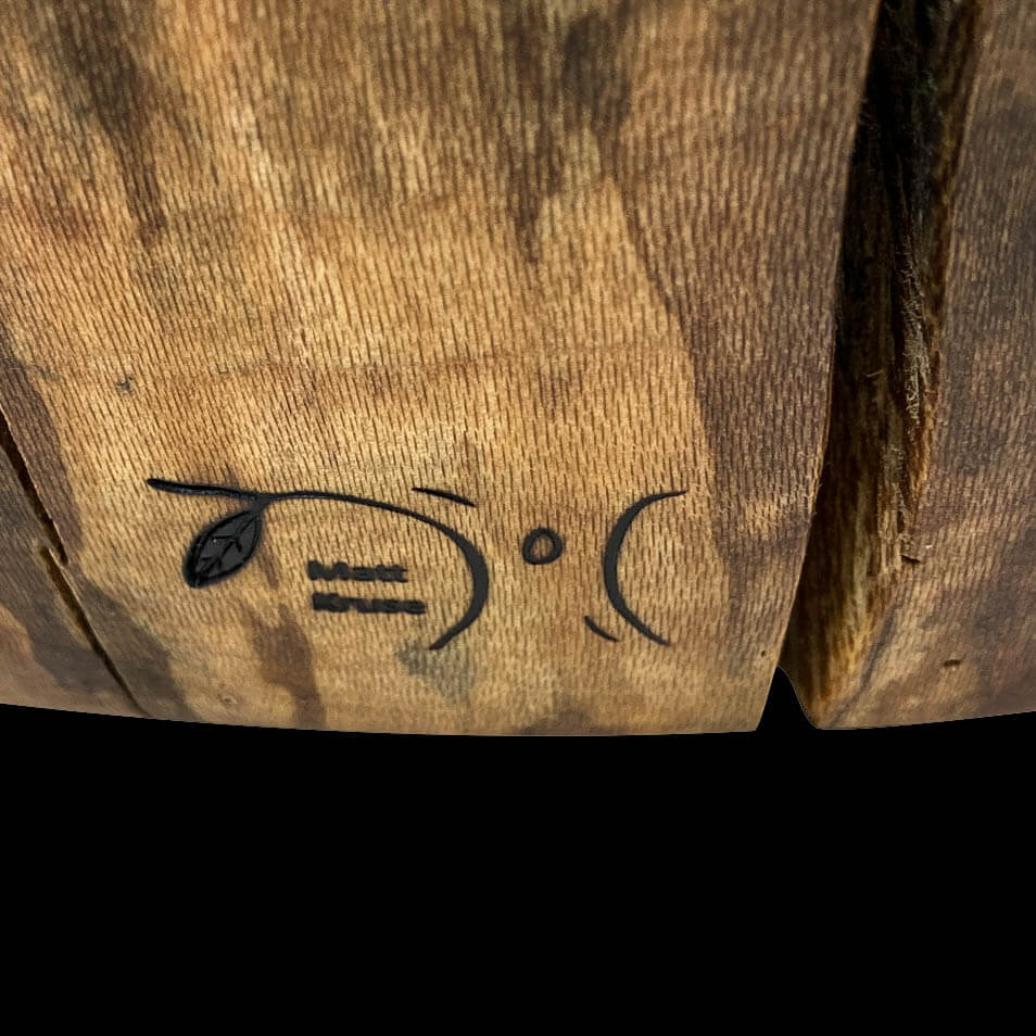 Base of chair with a heat brand of Ingrained Elegance.  A tree and leaf with name of artisan beneath.  Black background.