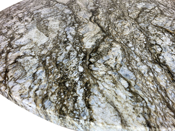 Close-up of a round blue dunes granite with gray, green, blue, and white colors streaking through out.