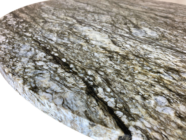 Close-up of rounded edge of a round blue dunes granite stone top with a dark vein running through white , green, and blue swirls.