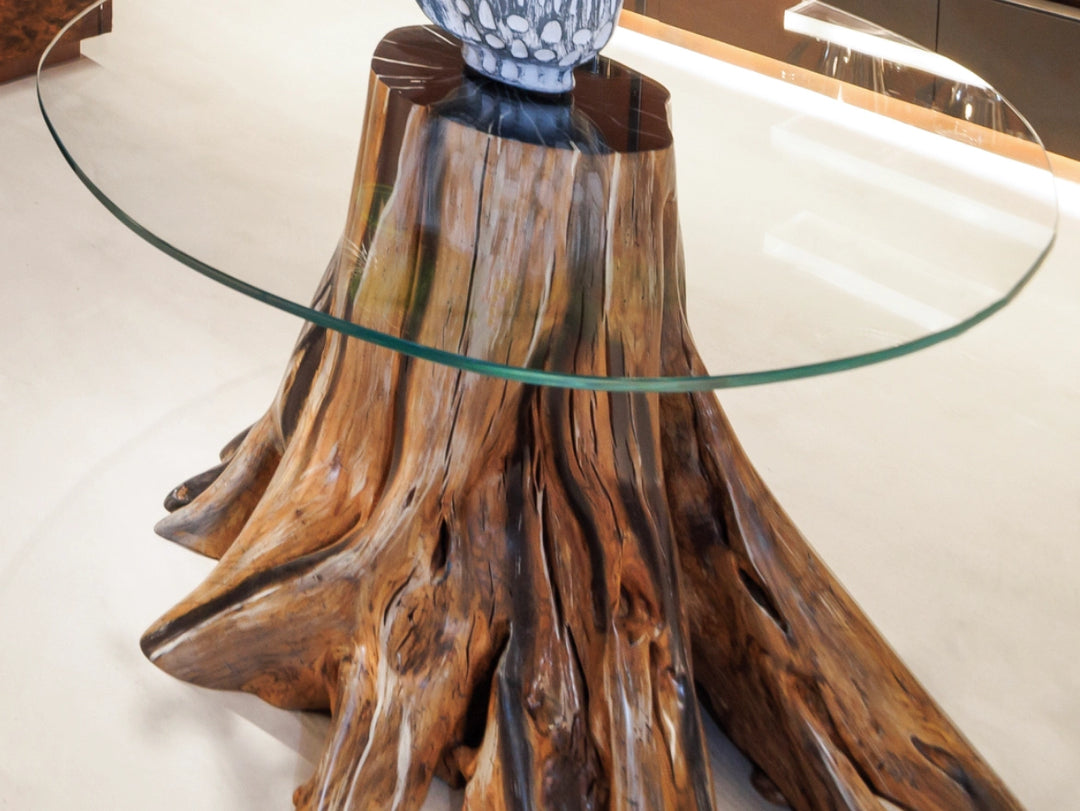 A rustic tree stump table base with a thick oval clear glass tabletop, used as a display table in a high end store.