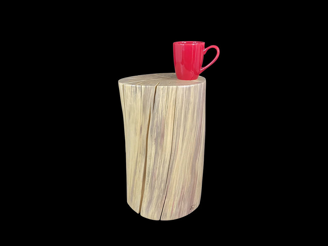 A rustic wooden side table made from a natural wood stump, shown against a solid black background with a small red ceramic mug resting on top.