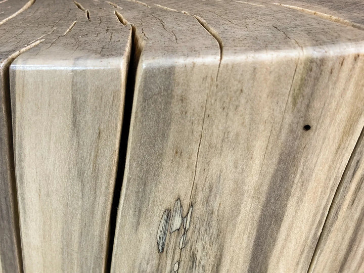 Close-up of a light natural wood surface of a log side table with visible grain, knots, and a vertical sanded split.