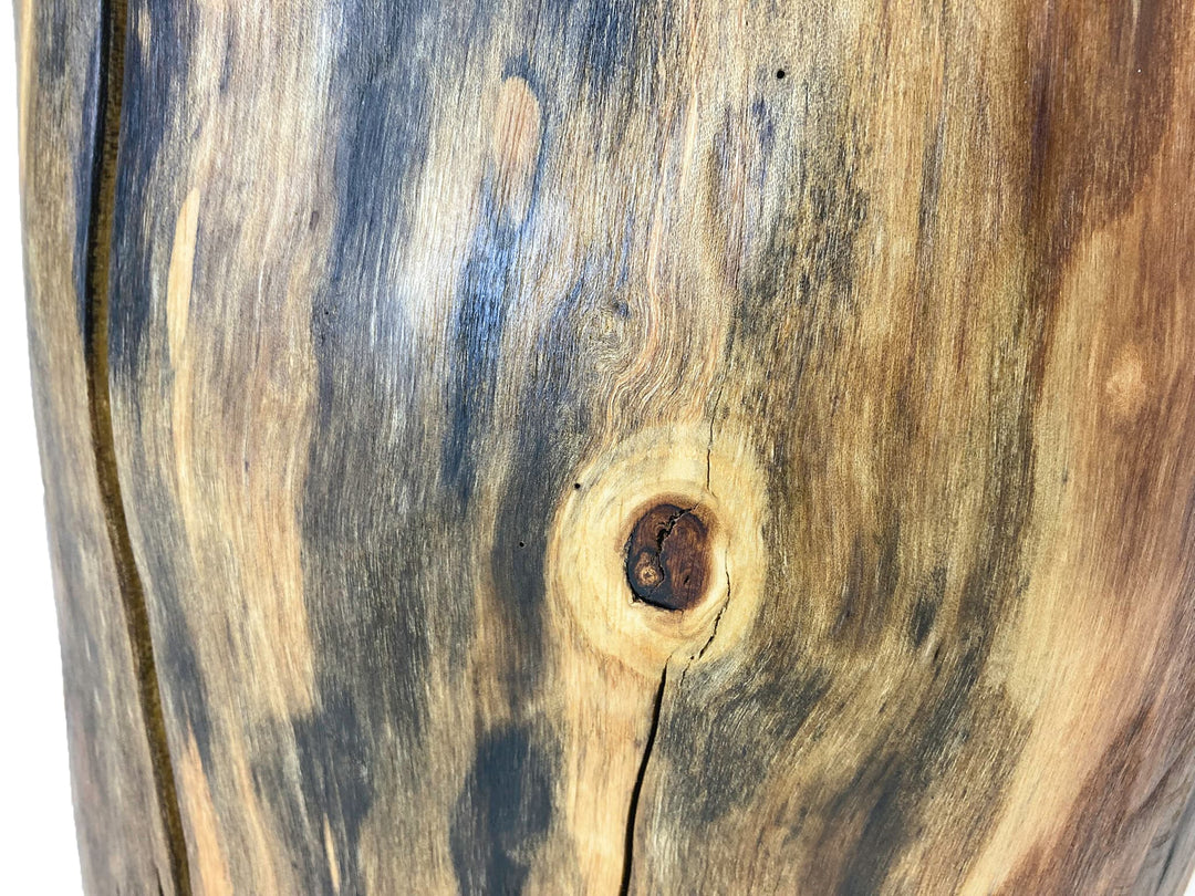 A close-up of a natural wood surface with prominent grain, including a visible knot and dark streaks, photographed against a white background.