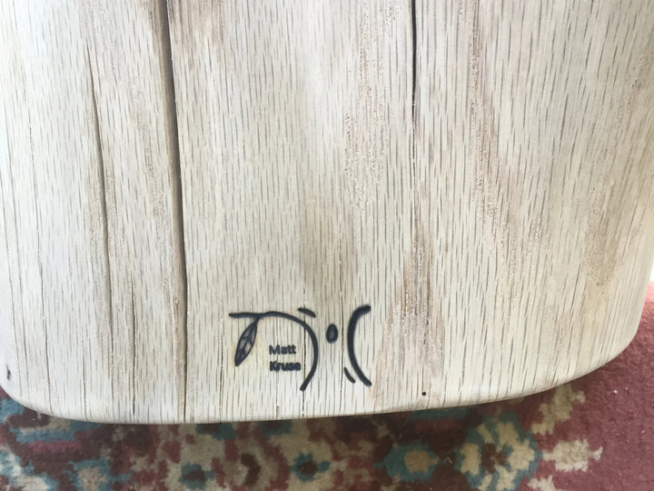 Close-up of an unfinished oak wood surface with a small black heat branded logo near the bottom center.