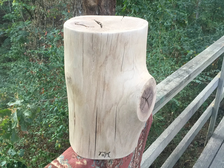 An oak side table in the unfinished stage set on a deck rail with a forest background.