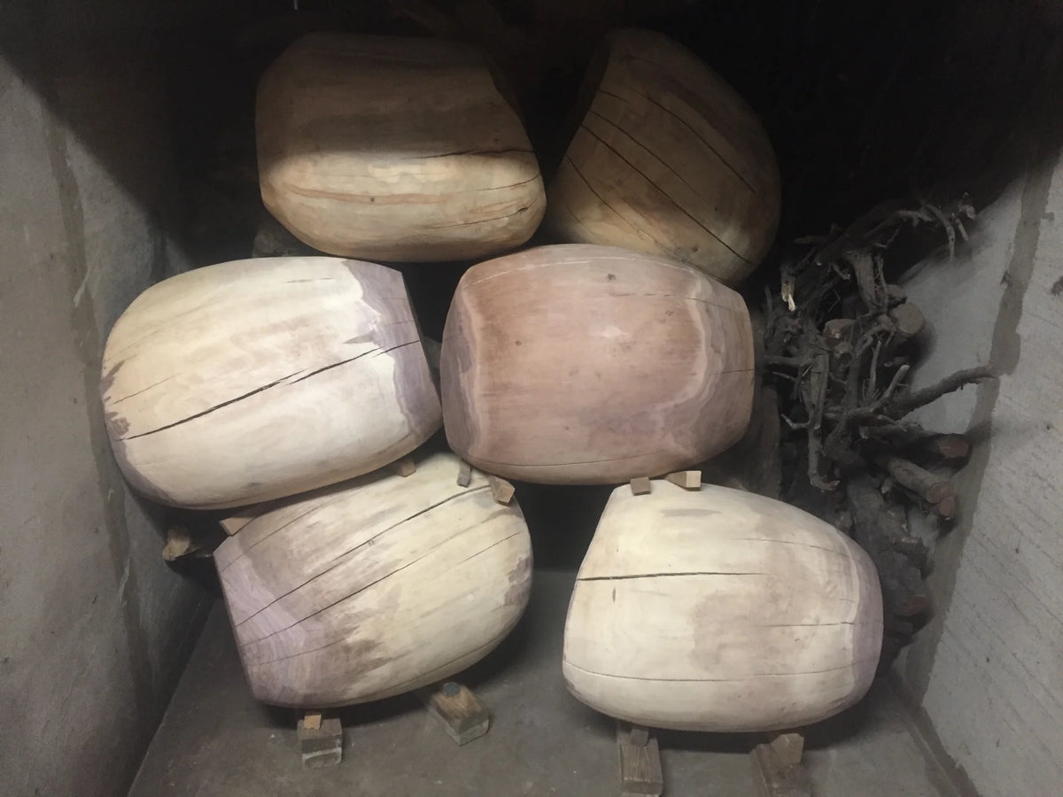 Six hand carved solid wood chairs and root structures stacked in a wood drying kiln made of cement board.