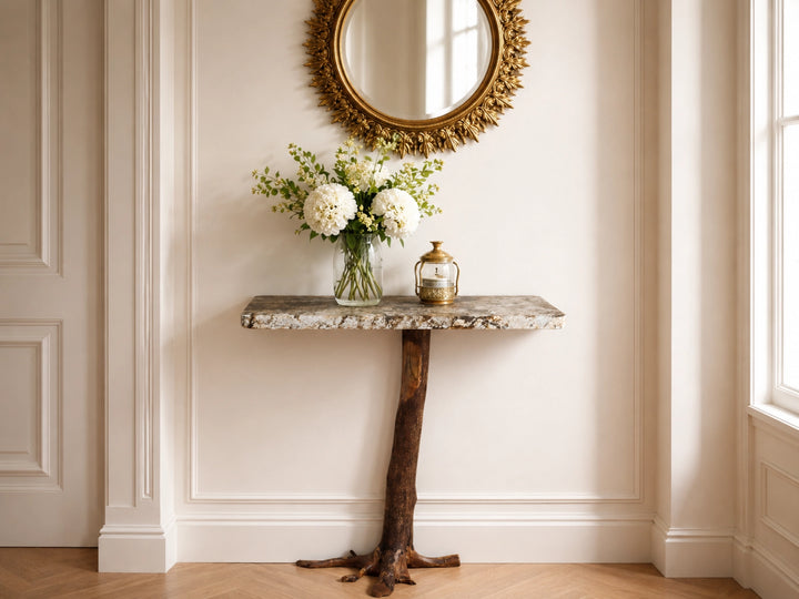 Staged view of a console table with a tree stump base against a luxurious home wall with a mirror above.