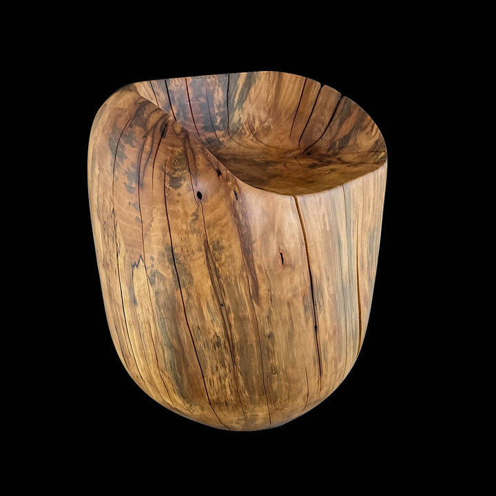 Angled view of solid hand carved sycamore chair.  Egg shape with a dip out of the top with black background.
