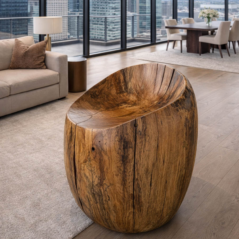 A solid hand carved vanity chair from sycamore in a high rise apartment living room with large glass windows showing city.  Gold and black wood patterns with a Matte finish with all natural Tung oil.  Wood floor and beige rug.