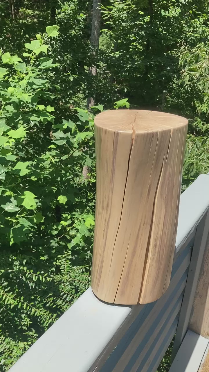 Video of a tan log side table on a grey deck rail with a forest in the back ground.